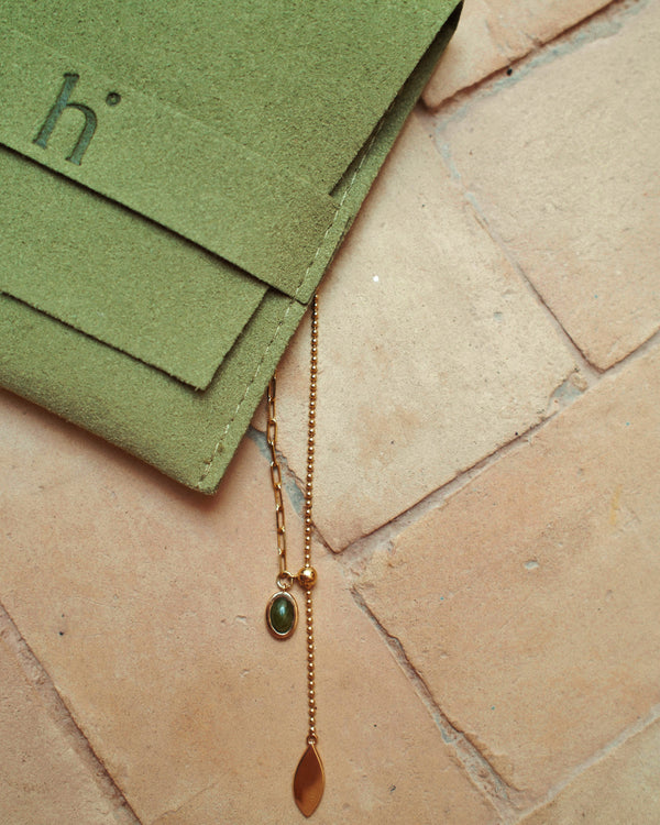 Gold necklace with a pendant on a textured stone surface next to green packaging with 'h' heiam branding.