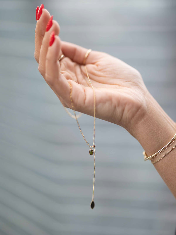 Hand wearing a gold necklace with a pendant against a blurred background